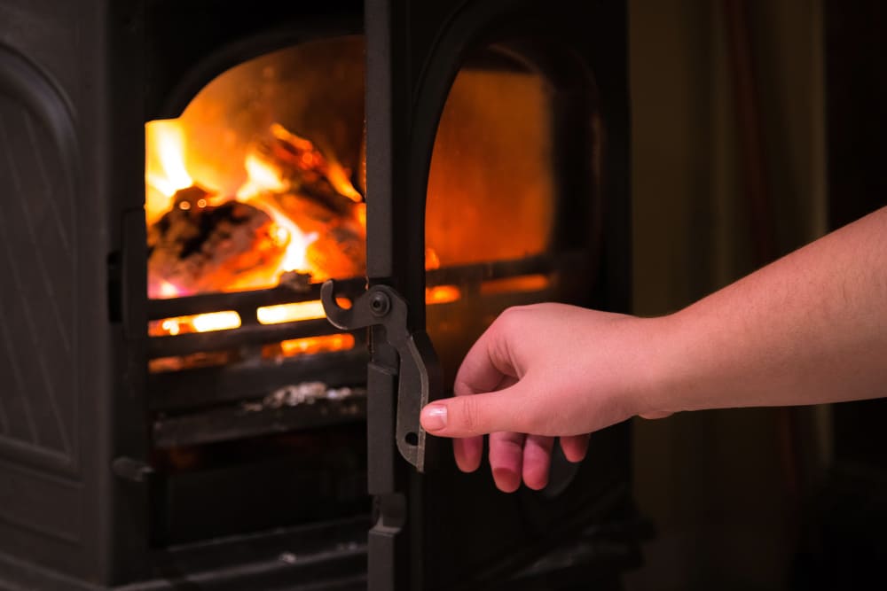 Hand opening the door of a burning wood stove